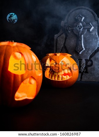Angry face and scared face of Halloween pumpkins with moon and tombstone on misty dark background.