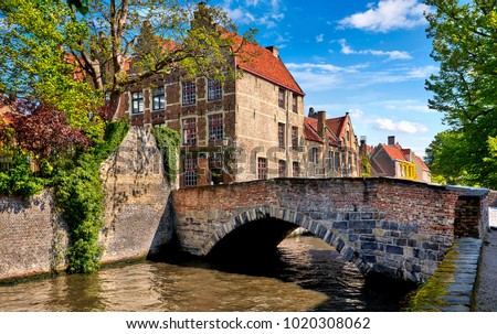 Bruges Belgium vintage stone houses and bridge over canal ancient medieval street picturesque landscape in summery sunny day with blue sky white clouds.