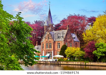 Bruges (Brugge), Belgium. Minnewater lake of love in picturesque park. Traditional ancient medieval castle with tower on bank among trees with red, pink, yellow and green crowns. Picturesque.