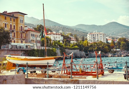Resort town Lovran, Croatia. Boat at piers by sea near coast. Mountains far away and blue sky. Summer seaside Croatian landscape with sunny day.