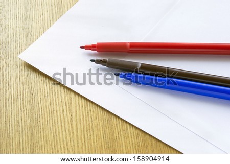Three multicolor felt pens and blank paper sheets on wooden desk