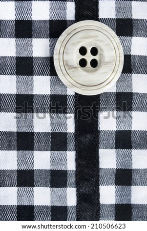 Big ivory button on black and white squared fabrics as a background