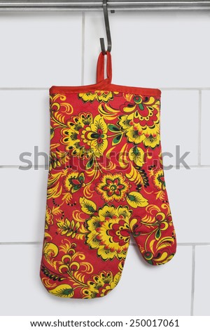 Red ornamental oven-glove hanging over brick wall as a background