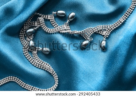 Silver pearl necklace on blue draped silk as a background