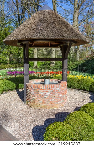 New water well with metal bucket in park with flowers