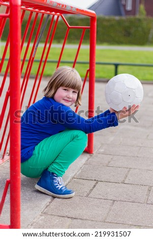 Young crouching girl with ball in red metal goal on schoolyard