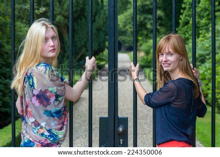 Two girls holding metal bars of entry gate of park