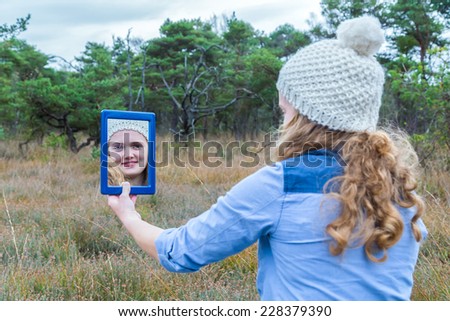 Blonde girl looking in mirror with forest background