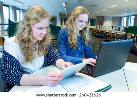 Two teenage girls working on computer and tablet in computer classroom