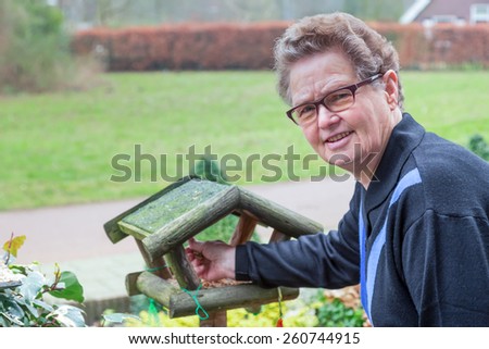 Elderly woman putting food in bird house outdoors