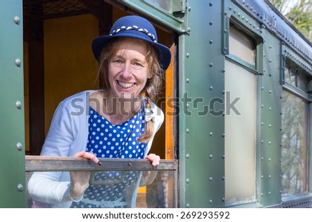 Dutch woman in old-fashioned clothes in open window of train. The caucasian middle aged woman wears a blue dress and a hat, she smiles at the camera. She\'s in an old carriage of a steam locomotive