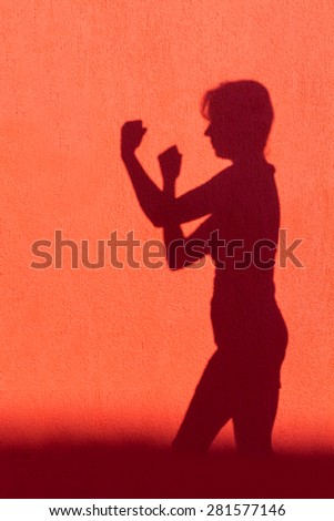 Shadow silhouette of woman showing fists projected on red wall