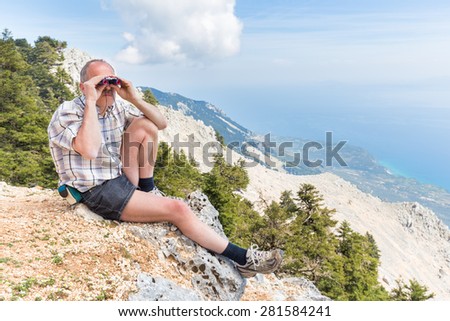 Man sitting in mountains looking through binoculars or spyglass