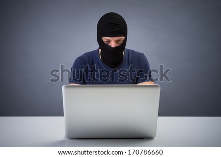 Computer hacker - Male thief stealing data from laptop. Studio portrait on grey background