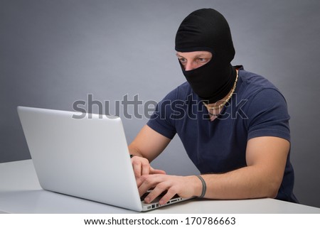 Computer hacker - Male thief stealing data from computer. Studio portrait on grey background