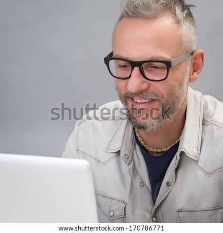 Smiling man with black glasses while is looking his notebook - Studio portrait on grey background
