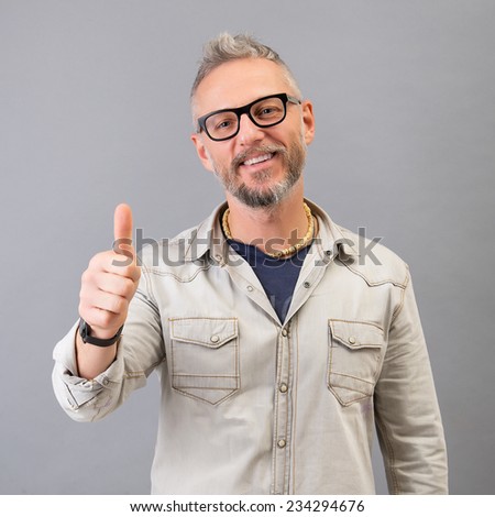 Closeup of young man with black glasses making the ok thumbs up hand sign. Studio portrait in gray background