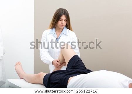 Female doctor physiotherapist practicing massage to her leg male patient in medical center.