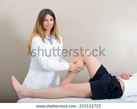 Female doctor physiotherapist smiling and practicing massage to her leg male patient in medical center.