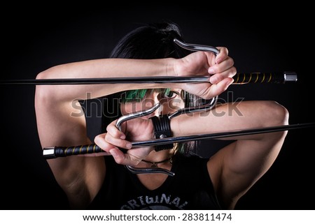 young woman in fighting stance holding a pair of sai: studio portrait on black background