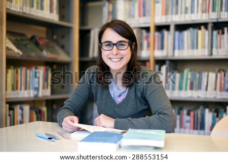 in the library - portrait of pretty female student with books while works and smiles
