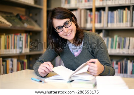 in the library - portrait of pretty female student with books while works and smiles