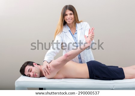 Female doctor physiotherapist smiling and practicing massage to her arm male patient in medical center.