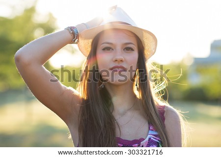 Beauty Romantic Girl Outdoors. Beautiful young brown hair model  dressing a white panama hat at park in Sun Light. Summer portrait. Glow Sun, Sunshine. Backlit. Toned in warm colors