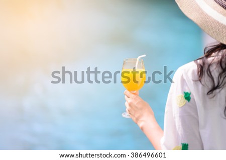 Rear view of beautiful woman in hat is holding orange juice glass at poolside in summer.