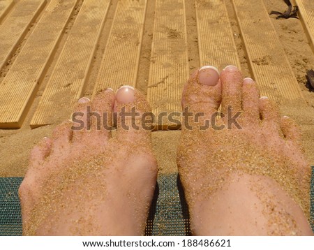Female feet/Beauty woman feet nails on sand. Wellness on beach.