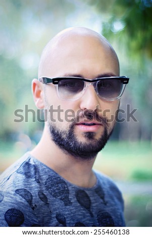 Shot of a handsome young man with beard and modern sunglasses/Attractive man in city park background