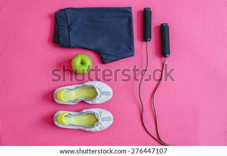 Sport shoes, apple, sweat suit and rope arranged  on pink sport mat. Top view angle/Sport equipment on pink mat