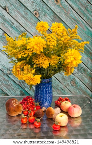 yellow flowers bouquet in a blue vase with apples and rose-hips