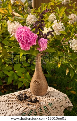 still life with pink hydrangea in a vase and white hydrangea plant as a background