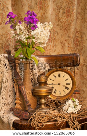 still life with phlox bouquet in a vintage vase on the old chair with antique clock and oil lamp