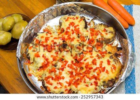 frying meat under the cheese laying on a round metal dish on a folio, pickled scallops on the plate and carrots on a wooden table