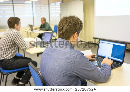 people sitting at the desks and printing on the keyboards of their notebooks in a training class and the coach at the backstage
