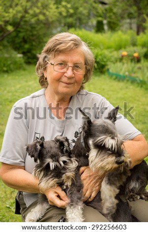 Senior woman hugs her two pets, black and silver miniature schnauzer dog in countryside