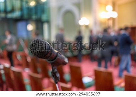 Microphone in focus against blurred chairs and standing talking audience