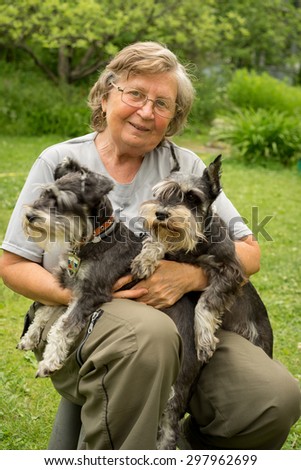 Senior happy woman in glasses and two black and silver miniature schnauzer dogs in a garden