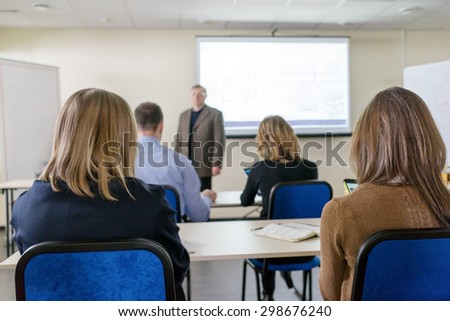people sitting rear at the desks in the class and teacher at the white screen