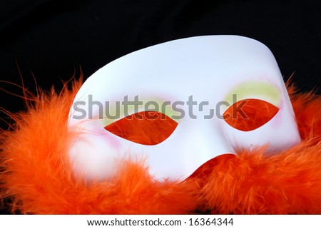 white plastic masqurade mask on an orange feather boa against a black background