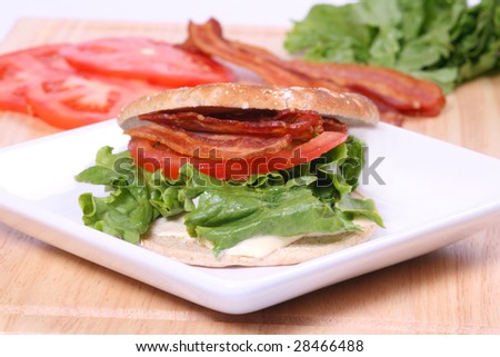 bacon lettuce and tomato sandwich on a flat roll with ingredients in the background