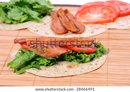 bacon lettuce and tomato sandwich on wrap with ingredients in the background