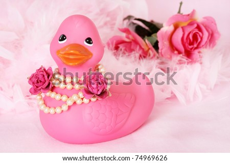 pink rubber duck with pearl necklace on, flowers and boa in the background on pink fabric.
