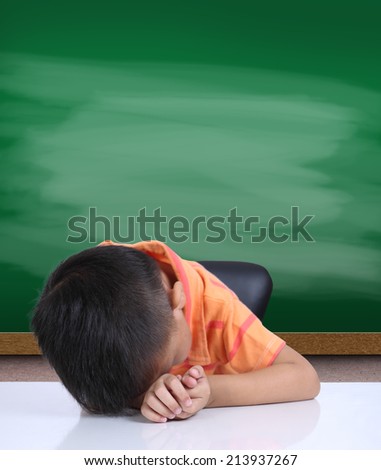 Little boy boring homework and sleeping on white table with Green chalk board,