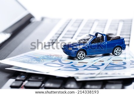 Toy car and banknotes over laptop keyboard