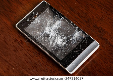 Broken smartphone with cracked display on wooden table
