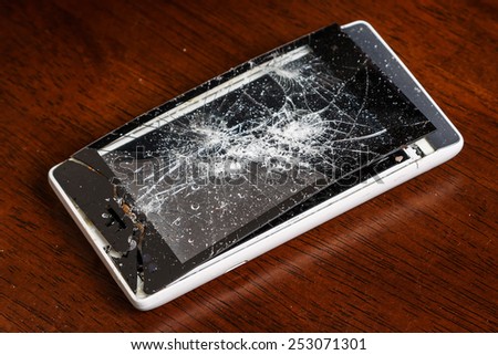 Broken smartphone with cracked display on wooden table