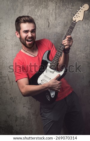 Handsome guy with electric guitar beside a dirty wall